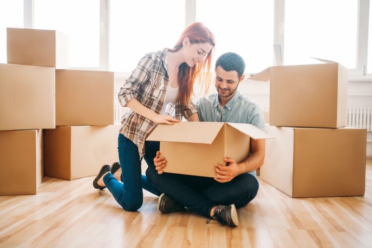 Happy couple unpacking carton boxes with property, housewarming. Moving to new house